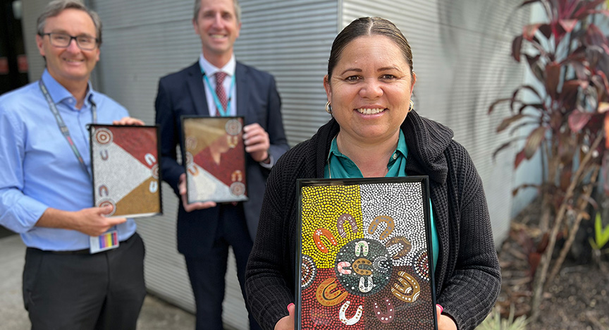 Three people holding framed First Nations artwork outside a building.