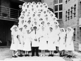 An old black and white photo of Princess Alexandra nurses and a doctor in traditional uniforms, standing outside a building.