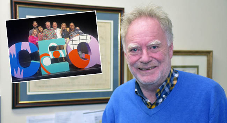 A person stands in an office with a framed photo of a group posing with large CEO letters.