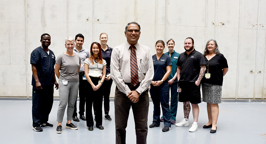 A group of healthcare workers stands together in a concrete-walled room, with one person in front wearing a tie.