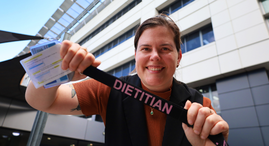 A person holding a DIETITIAN lanyard and a document in front of a modern building.