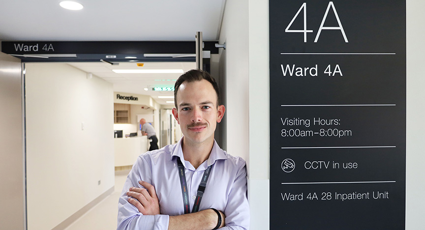 A person stands in front of the entrance to Ward 4A. The sign indicates visiting hours from 8:00am to 8:00pm and mentions CCTV in use.