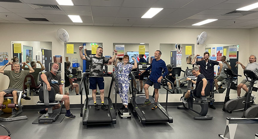 A group of people exercising on various gym equipment in a fitness room, with motivational posters on the walls.