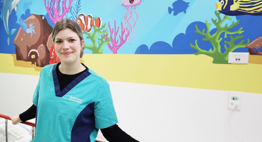 An undergraduate student in nursing standing in front of a colourful mural in the emergency department at Beaudesert Hospital