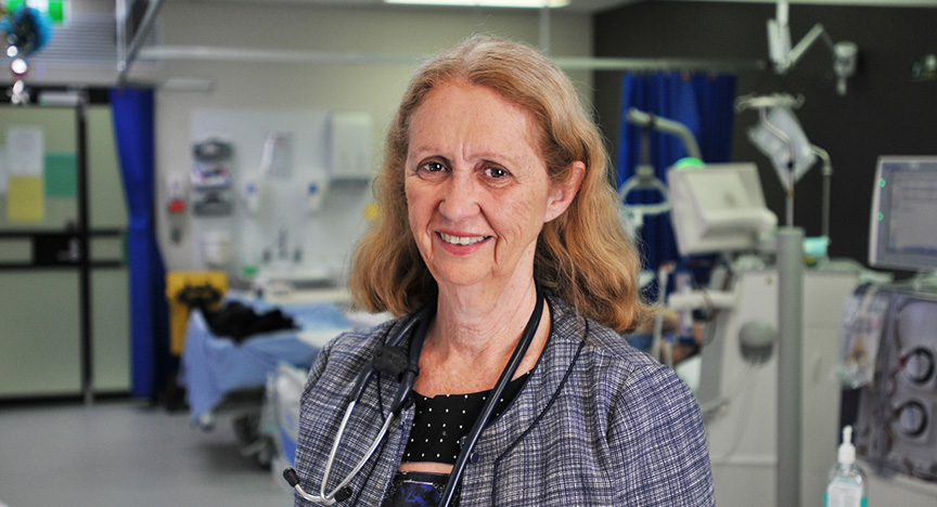 A healthcare professional with a stethoscope stands in a hospital room with medical equipment in the background.