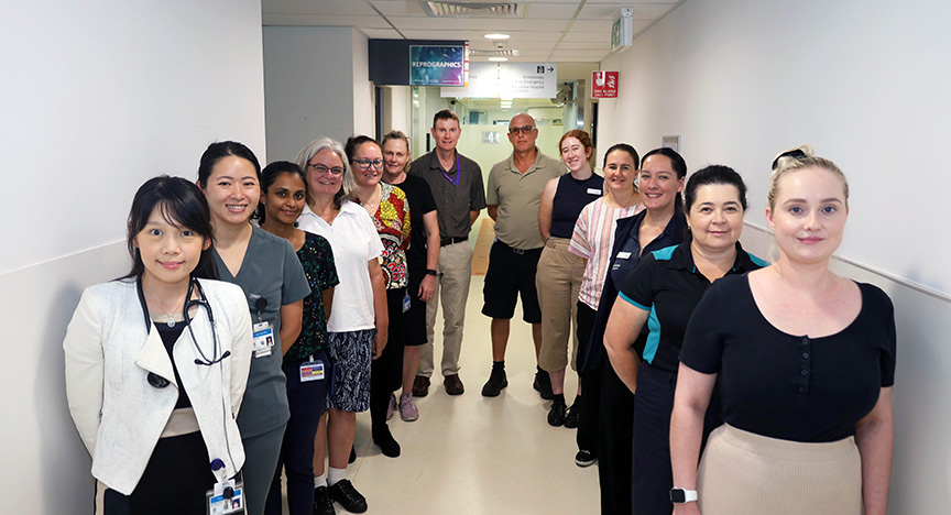 A group of healthcare professionals standing in a hospital corridor, some wearing uniforms and ID badges.