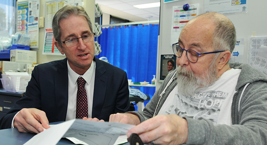 A person in a suit and another in casual clothing review documents in a medical office.