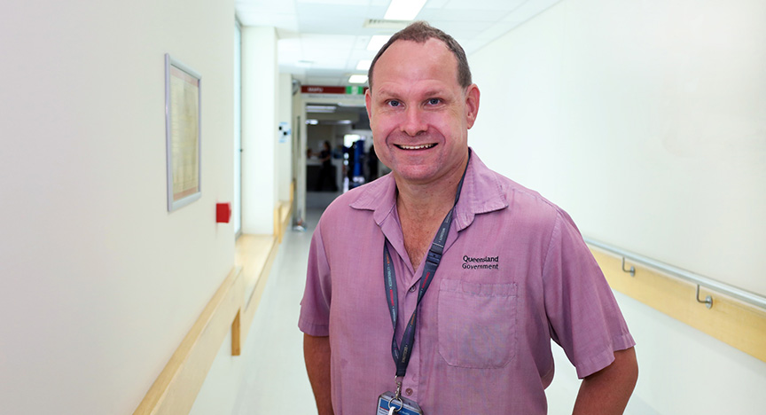 A person in a Queensland Government shirt stands in a hospital hallway.