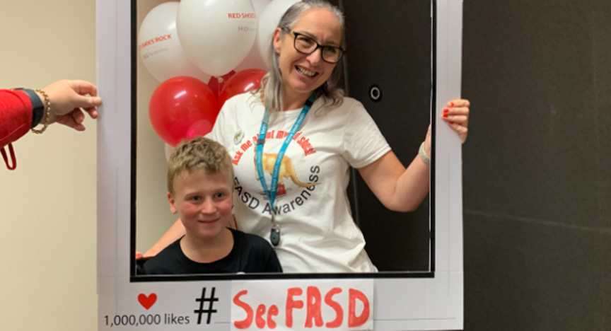 Two people holding a frame with See FASD text, promoting FASD awareness. Red and white balloons in the background.