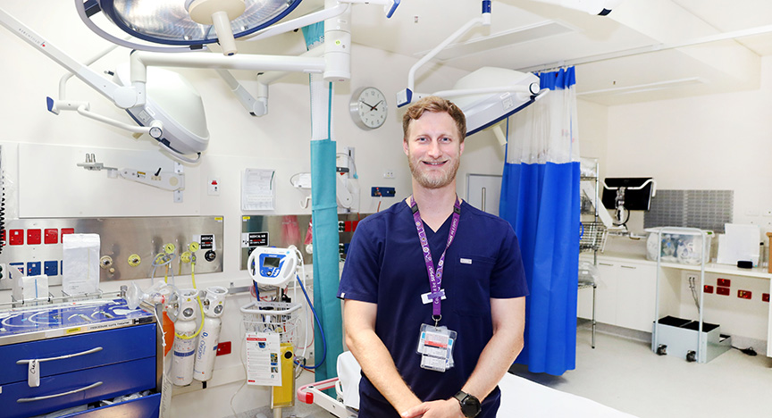 A healthcare professional stands in a well-equipped hospital room with medical devices and monitors.