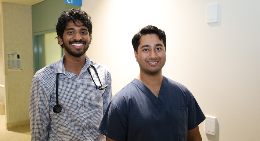 Two healthcare professionals stand in a hospital corridor, one wearing a stethoscope and the other in scrubs, near a sign labeled CT.