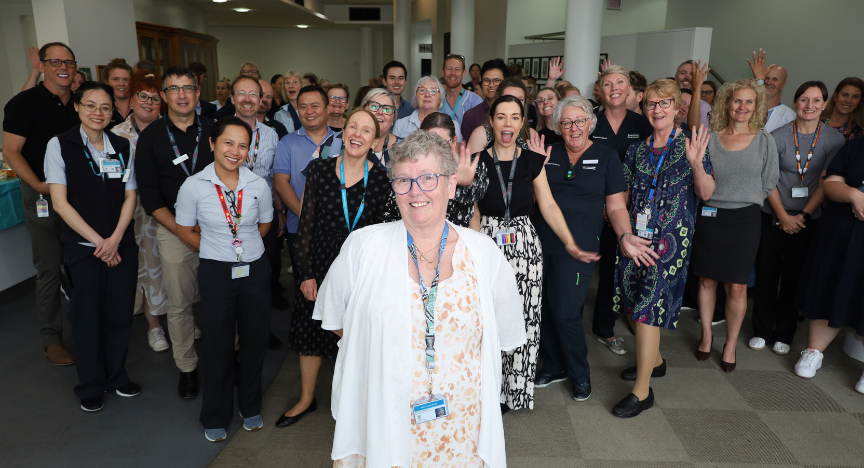 A group of healthcare professionals standing together in a hospital setting, some raising their hands, celebrating an event.