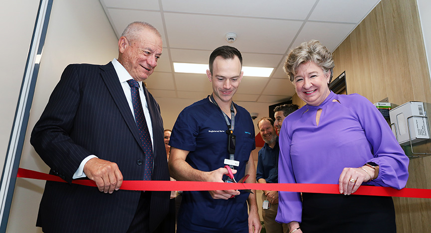 Three people cutting a red ribbon at a hospital ward opening ceremony.