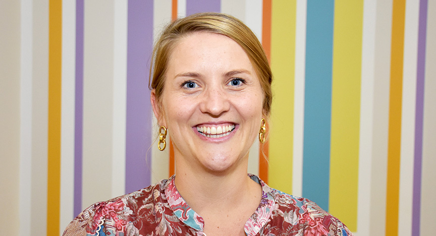 A person wearing a floral shirt stands in front of a colorful striped background.