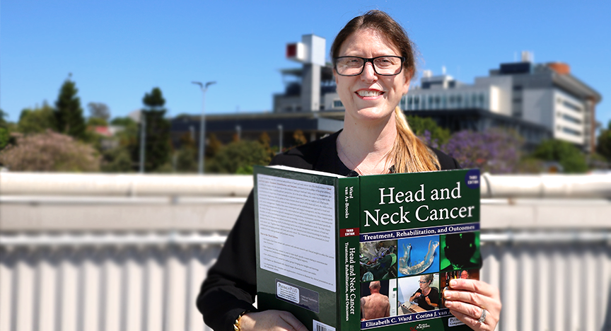 A person holding a textbook titled Head and Neck Cancer: Treatment, Rehabilitation, and Outcomes with a building in the background.