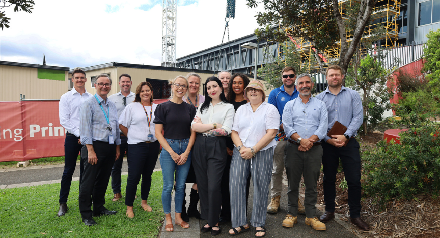 a group of hospital, construction and community representatives standing outside nearby to a construction site at PA Hospital with a crane towering in the background 