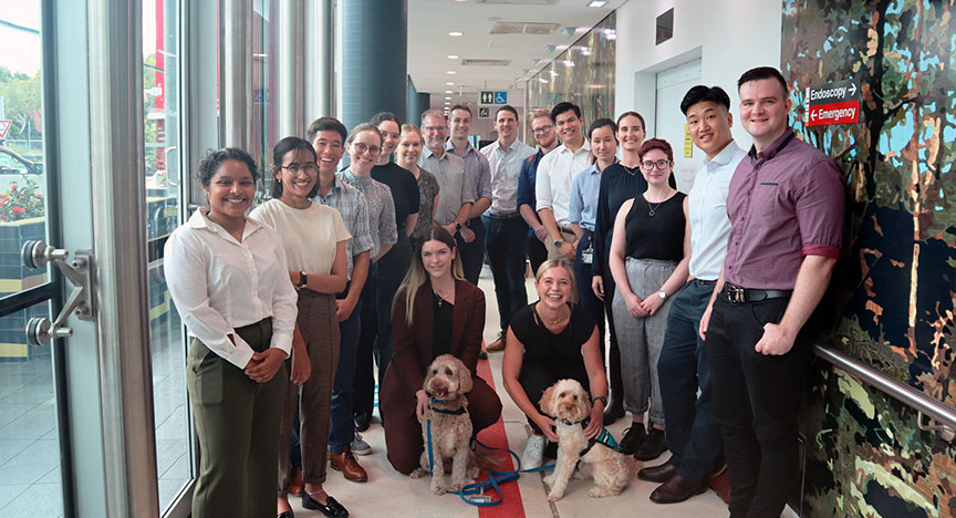 A group of people, some with guide dogs, standing in a hospital corridor near signs for Endoscopy and Emergency.