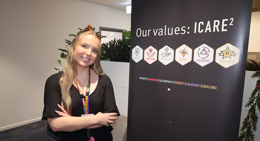 A person stands next to a banner displaying the values: Integrity, Compassion, Accountability, Respect, Engagement, and Excellence.