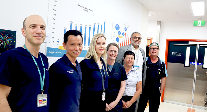 A group of healthcare professionals stands in front of charts and graphs in a hospital hallway.