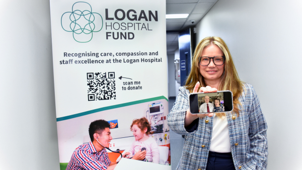 A person holds a phone displaying a photo in front of a Logan Hospital Fund banner, promoting care, compassion, and staff excellence.