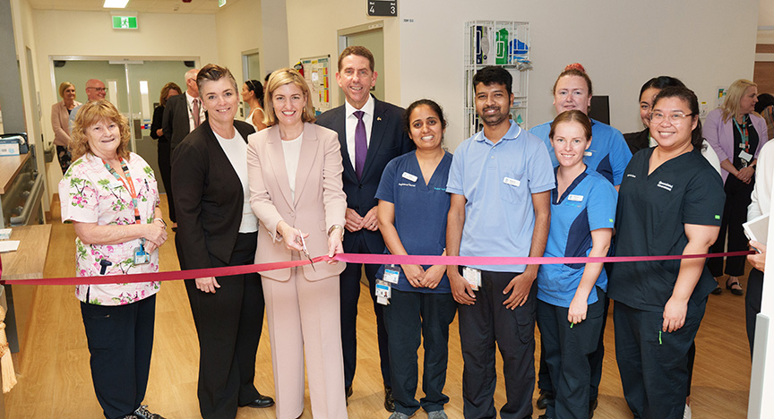 A group of healthcare professionals and officials cutting a red ribbon at the opening of a new ward in a hospital.