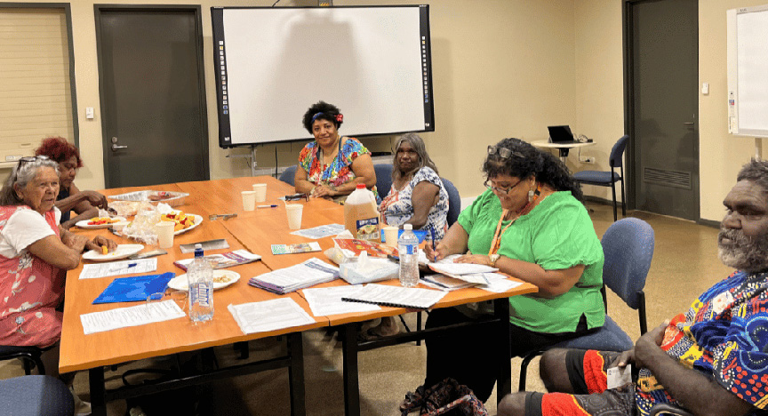 A group of First Nations people sitting around a table with papers and food, engaged in a discussion in a meeting room.