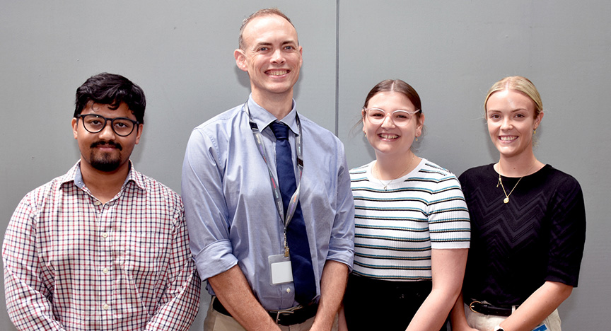 Four people standing side by side against a gray wall, dressed in business casual attire.