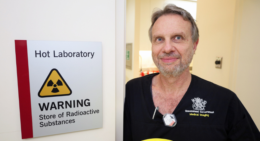 A person in a medical uniform stands next to a sign reading Hot Laboratory WARNING Store of Radioactive Substances.