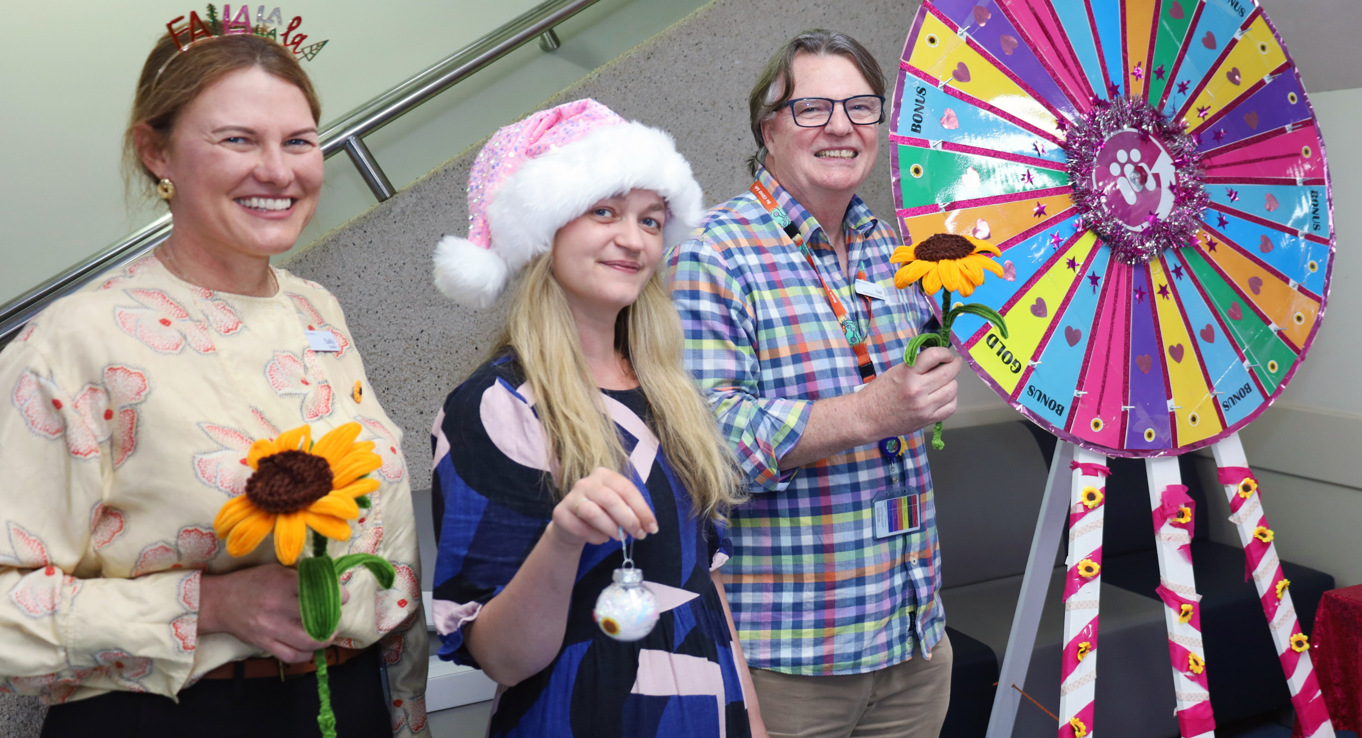 3 QEII staff members holding sunflowers next to giant wheel