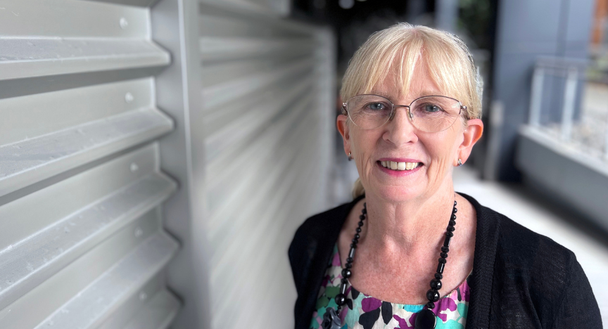 Mary Boyde, wearing glasses, stands in front of a wall at PA Hospital, exuding confidence and professionalism