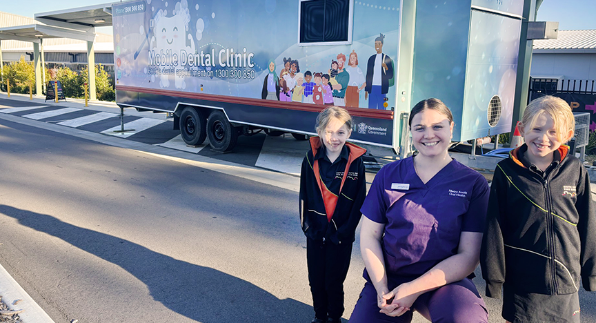 A mobile dental clinic parked on a street with three people standing in front of it, including a person in purple scrubs.