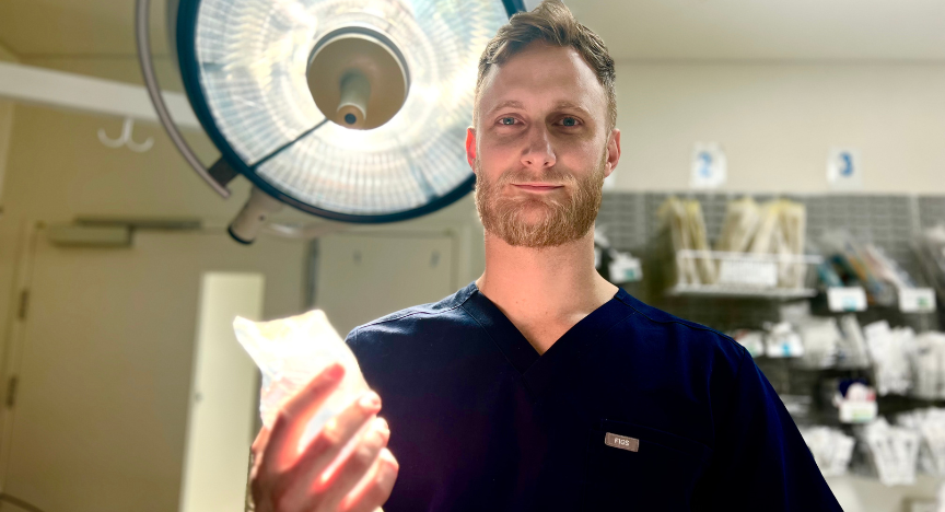 A healthcare professional in a dark blue uniform holds a medical item under a surgical light in a clinical setting.