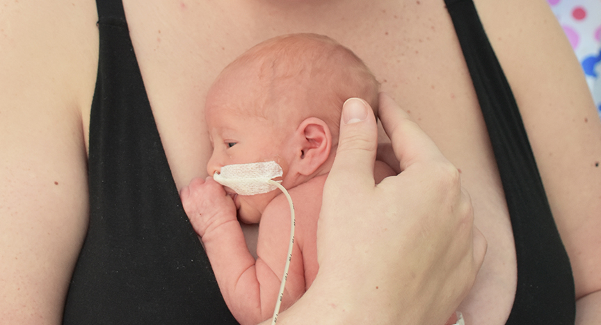 A person in a black top holds a newborn baby close to their chest, providing skin-to-skin contact.