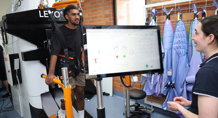 Spinal patient using the lexo machine with staff member standing at front screen