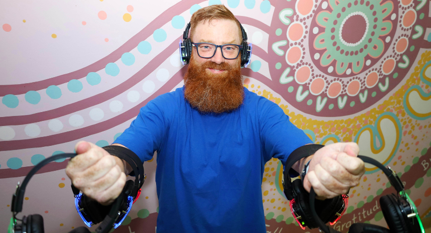 A person in a blue shirt holds two sets of headphones in front of a colorful, patterned wall.