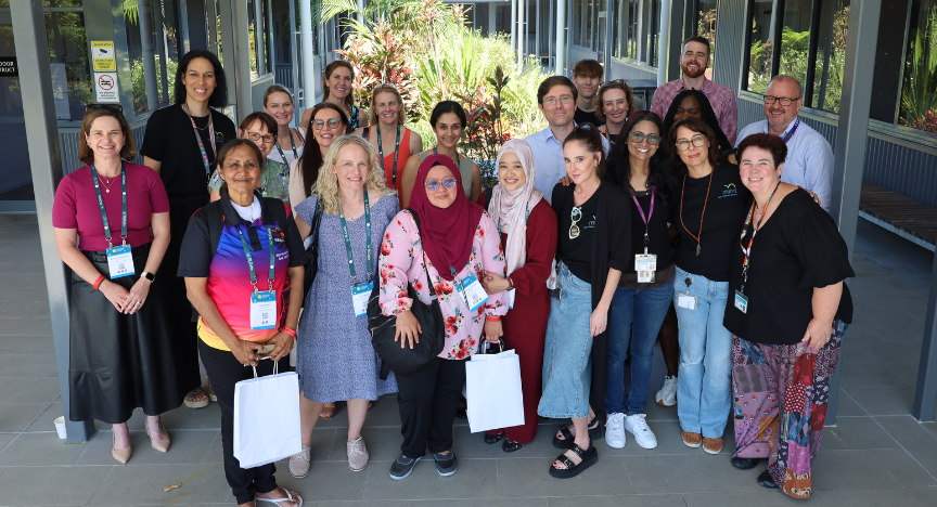 Group of around 20 mental health professionals standing outside health clinic in front of garden with some holding white bags