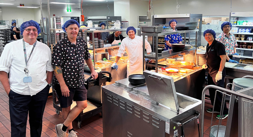 A variety of food services staff standing in PA Hospital kitchen during lunch service