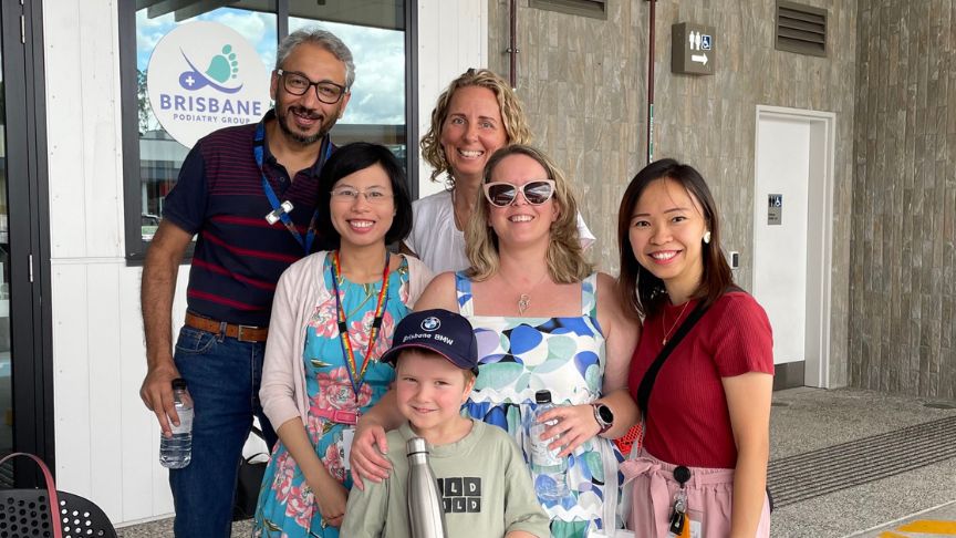 A small group of smiling people dressed in casual clothes. The group is made up of healthcare workers and a mother and son from the community. The child is wearing a hat, the mother sunglasses and they are both holding a water bottle.